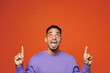 © ViDi Studio - Young fun man of African American ethnicity wear purple sweatshirt casual clothes point index finger overhead on area mockup isolated on plain red orange background studio portrait. Lifestyle concept.