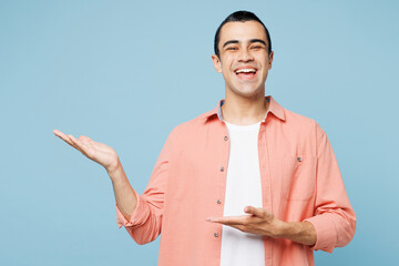 Poster - Young smiling fun happy cheerful middle eastern man he wears pink shirt white t-shirt point hands arms on y area isolated on plain pastel light blue cyan background studio portrait. Lifestyle concept.