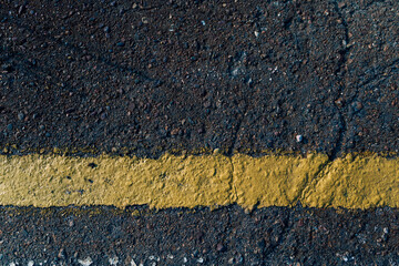 Close-up of a cracked asphalt road with yellow line