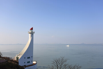 Wall Mural - Haenam-gun, Jindo-gun, Jeollanam-do, South Korea - December 15, 2021: Winter view of Mokpo Old Lighthouse against a ship sailing on the sea