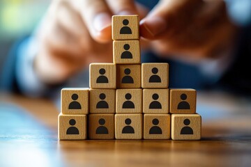 Building a Strong Team:  A hand carefully places a wooden block with a person icon on top of a pyramid structure, symbolizing the importance of building a strong team for success.