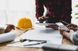 © Wasan - Brainstorming group of architects and engineers discuss building blueprint design paperwork and drawing construction project planning on wooden table in office. Construction project budget planning.
