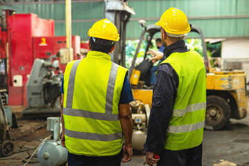 Two men in yellow safety vests stand next to a forklift