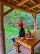 © Valeriia - Woman in red hat and green tracksuit sits near rustic wooden cabin with cup, pastries in the morning