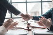 © ArLawKa - Close-up of a male lawyer making a deal and shaking hands with a male client at the table in his office. Office with judge's gavel and scale on table. Law