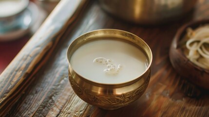 Canvas Print - A golden bowl filled with white liquid,  resting on a wooden table.