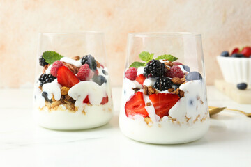 Wall Mural - Tasty yogurt with fresh berries, granola and mint in glasses on white marble table