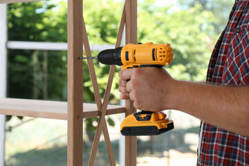 Canvas Print - Man with electric screwdriver assembling furniture indoors, closeup