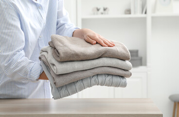 Sticker - Woman with stack of clean clothes at wooden table indoors, closeup