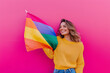 © Роман Варнава - Joyful woman waves an LGBT flag in front of a vibrant pink wall, celebrating diversity