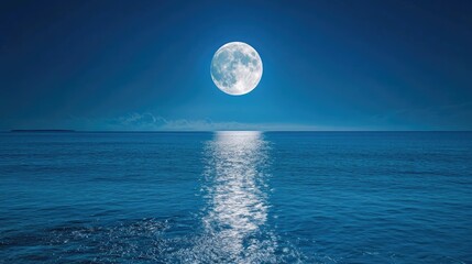 The full moon illuminates the clear blue sky, its light reflecting softly on the calm ocean waters below, creating a tranquil scene.