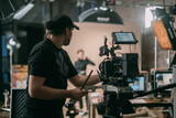 Director of photography with a camera in his hands on the set. Professional videographer at work on filming a movie, commercial or TV series. Filming process indoors, studio