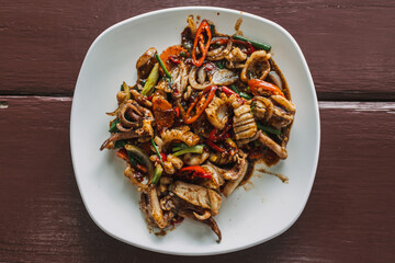 Thai Stir-fried squid with black pepper on white dish served on the table.