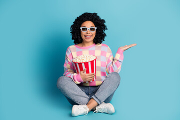 Full size photo of young girl watch movie eat popcorn hold empty space wear trendy pink plaid outfit isolated on blue color background