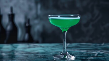 A single cocktail glass filled with bright green liquid sits on a blue-green surface.