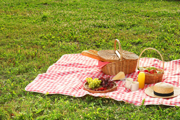 Wall Mural - Picnic basket, different snacks, juice and straw hat on red checkered blanket outdoors