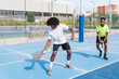 © Koldo_Studio - Two African teammates strategizing and enjoying a fun game of pickleball on a bright, sunny day.