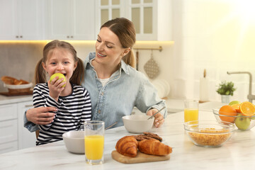 Canvas Print - Mother and her cute little daughter having breakfast at table in kitchen on sunny morning