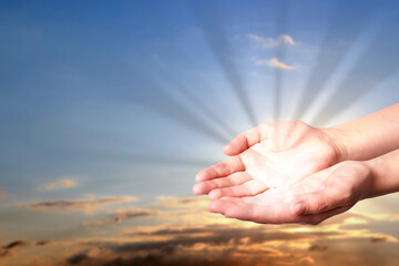 Woman with holy light in hands against sky on sunrise, closeup