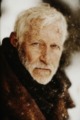 An elderly man with white hair and a weathered face stands in a rugged, possibly wintry setting. His intense gaze and visible experience reflect a life of adventure.