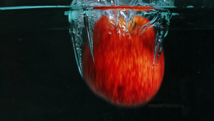 A close up of a fresh vibrant red tomato floating in clear water with black background. Macrography of organic apple falling and dropping in to splashing cool water. Freshness concept. Pabulum.