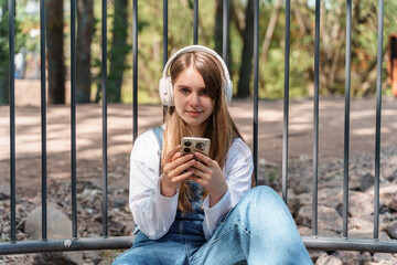 A young teenage girl wearing headphones romantically mysteriously looks away at sunset and walks in a city park. 