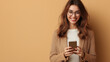 © zineb - Cheerful young woman in smart casual outfit using her smartphone. She is standing against a neutral background, smiling confidently, conveying positivity and modern professionalism.
