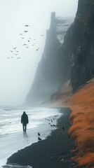 Wall Mural - Solitary person walks along a misty beach with birds flying, beside dramatic cliffs and vibrant orange grasses