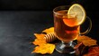 © fivan - A glass of dark rum hot toddy with a lemon slice and honey drizzle, set against a deep charcoal background with golden autumn leaves