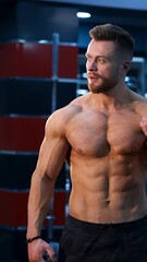 Wall Mural - Muscle athlete strongman pumps muscules in a gym after heavy training. Perfect torso with strong abs. Handsome power male with naked torso. Vertical video