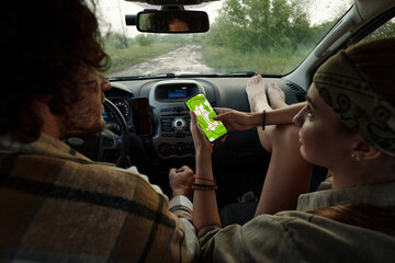 Young female backpacker keeping bare feet on front part of air ventilation grille during discussion of mobile map app with driver