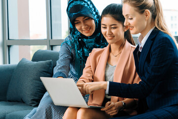 Wall Mural - Multicultural working group. Team of businesswomen of different ethnicity, Caucasian, Asian and Arabic working together with laptop computer at office workplace. Multiethnic teamwork concept. uds