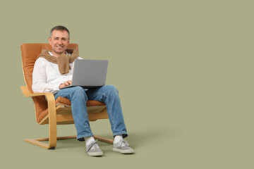 Wall Mural - Mature man with laptop messaging in armchair on green background