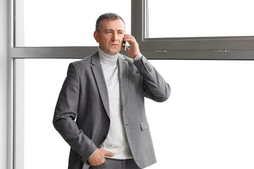 Wall Mural - Mature businessman talking by mobile phone in office