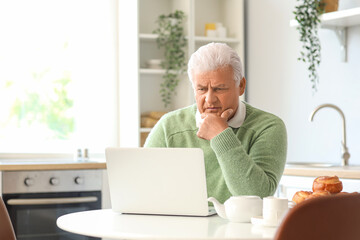 Canvas Print - Thoughtful senior man using laptop in kitchen