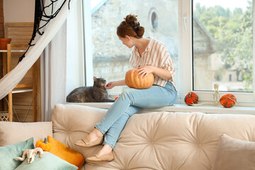 Sticker - Young woman with cute cat and Halloween pumpkins on windowsill at home