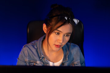 Portrait young beautiful Asian creative with serious face looking on pc to search project creator social media online, planning new strategy creator at neon modern office at night time. Stratagem.