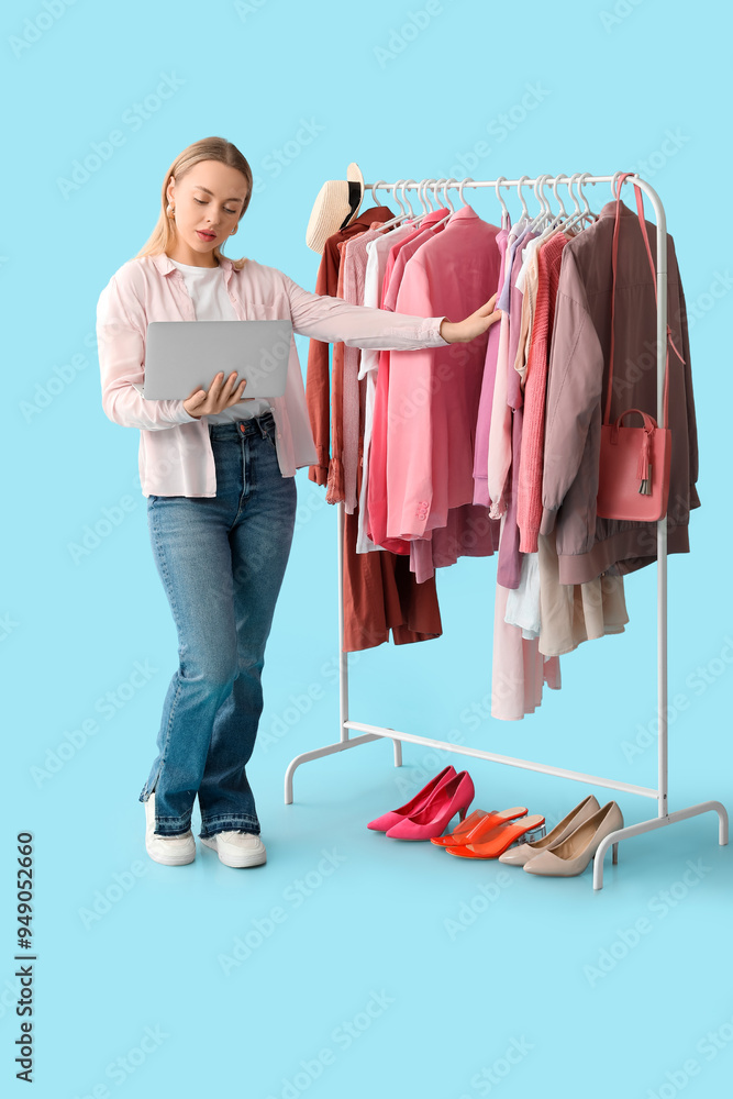 Female stylist with laptop and on rack against blue background