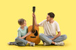 © Pixel-Shot - Private music teacher and little boy with guitar sitting on yellow background