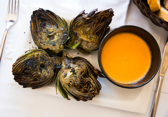 Wall Mural - Top view of traditional Catalan vegetarian appetizer of grilled artichokes on white plate with piquant romesco..