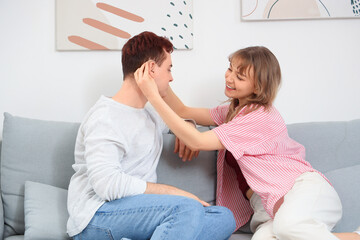 Wall Mural - Young couple putting hearing aid on sofa at home