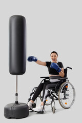 Poster - Female boxer in wheelchair with punching bag on light background