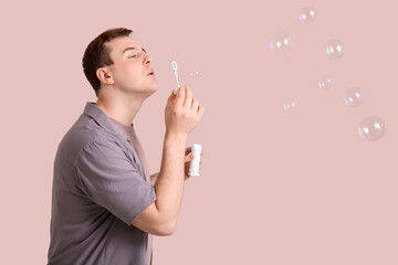 Wall Mural - Young man blowing soap bubbles on pink background