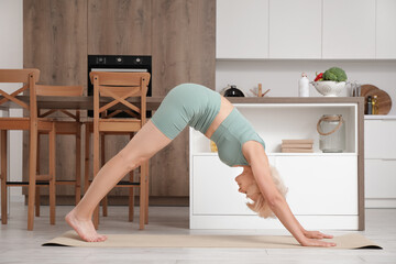 Poster - Sporty beautiful mature woman practicing yoga and stretching in kitchen at home