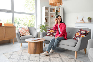 Wall Mural - Young woman in eyeglasses sitting on sofa at home