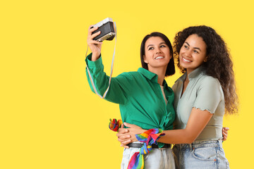 Wall Mural - Young lesbian couple taking selfie on yellow background