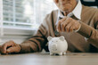 © Pcess609 - Saving money investment for future. old man hand putting money coins in a piggy bank.investment, money, annuity insurance, saving for retirement and pension fund concept.Individual retirement account.