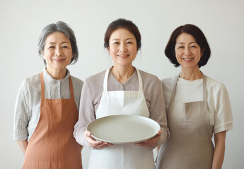 Wall Mural - Three Japanese women wearing aprons stand smilingly in front of the camera. One woman is holding a cracked plate