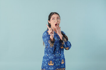 Wall Mural - Surprised government worker woman in blue batik uniform pointing to the copy space behind her.