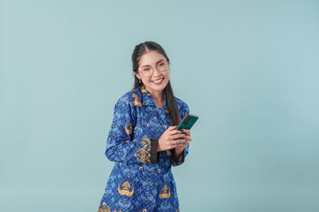 Excited government worker woman wearing blue batik uniform and glasses holding a smartphone.